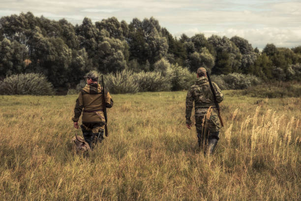 Hunters men going through rural field towards forest during hunting season